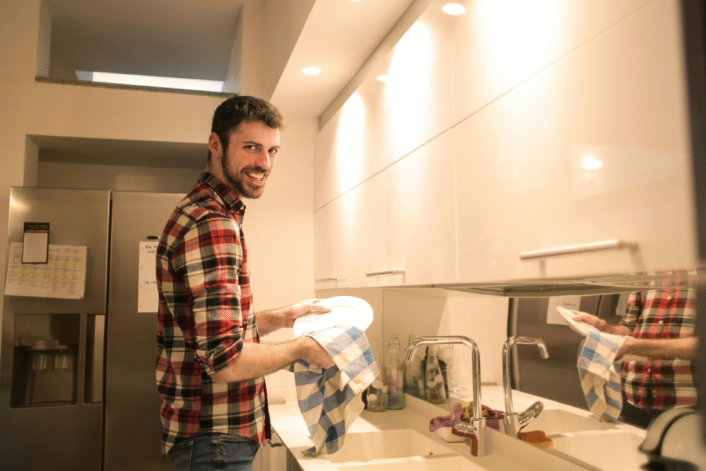 A man smiling while cleaning dishes, showing one way to counter laziness.